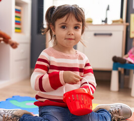 Adorable hispanic girl playing supermarket game sitting on floor at kindergarten