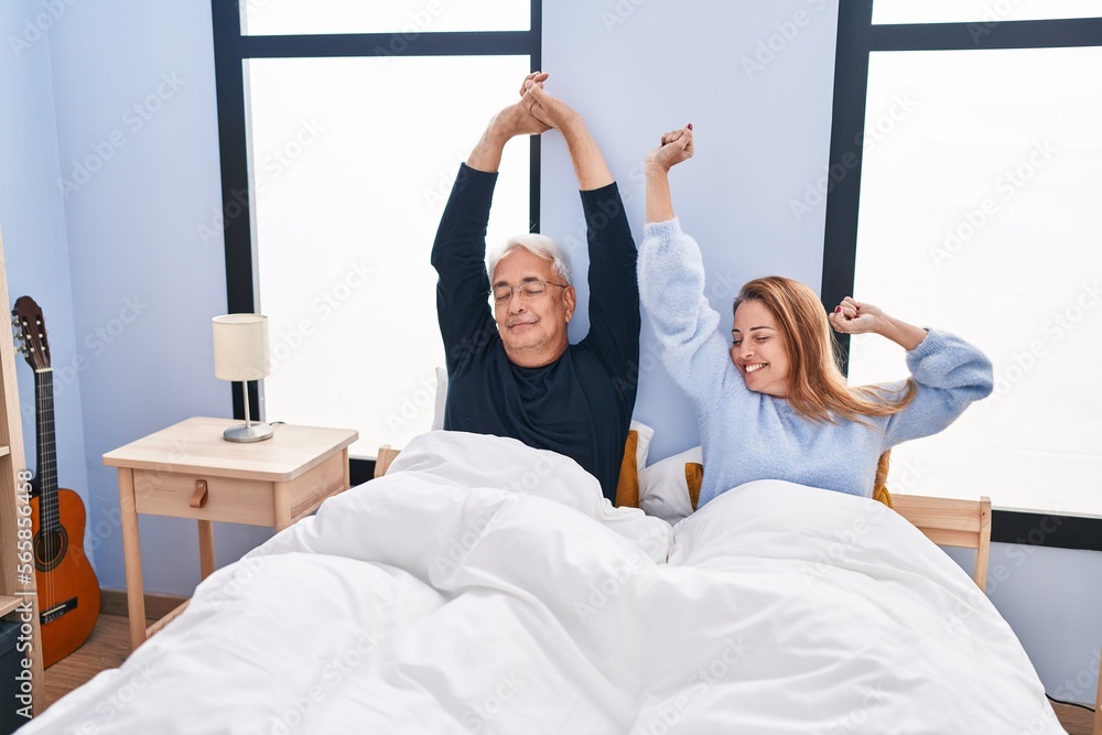 Poster middle age man and woman couple stretching arms lying on bed at bedroom