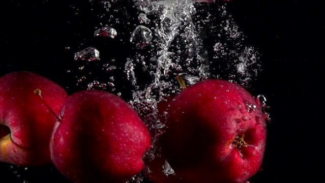 Slow motion red apple falling underwater water on black background. Beautiful fresh fruit splashing in aquarium. Organic fruits, healthy food, diet, concept. Filmed at high speed camera at 4k 1000 fps
