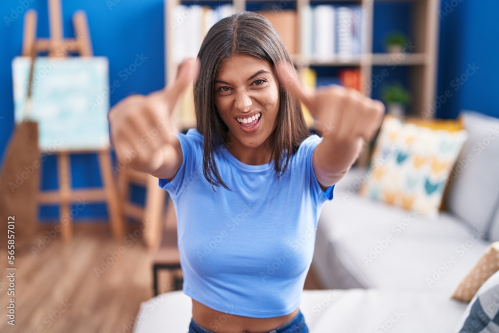 Poster brunette young woman sitting on the sofa at home approving doing positive gesture with hand, thumbs 