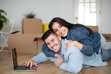 Happy Young Spouses Embracing And Using Laptop After Moving To Their New Home,