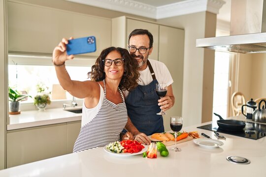 Middle age hispanic couple smiling confident cooking and make selfie by the smartphone at kitchen