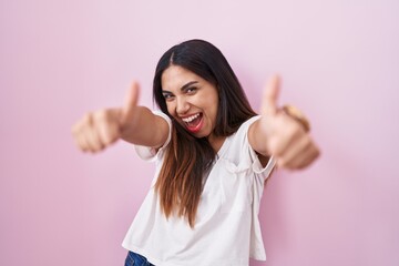 Young arab woman standing over pink background approving doing positive gesture with hand, thumbs up smiling and happy for success. winner gesture.