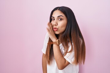 Young arab woman standing over pink background hand on mouth telling secret rumor, whispering...
