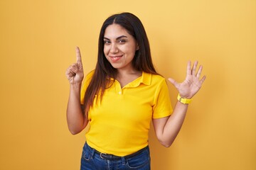 Young arab woman standing over yellow background showing and pointing up with fingers number six while smiling confident and happy.