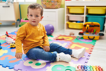 Adorable caucasian boy playing xylophone sitting on floor at kindergarten