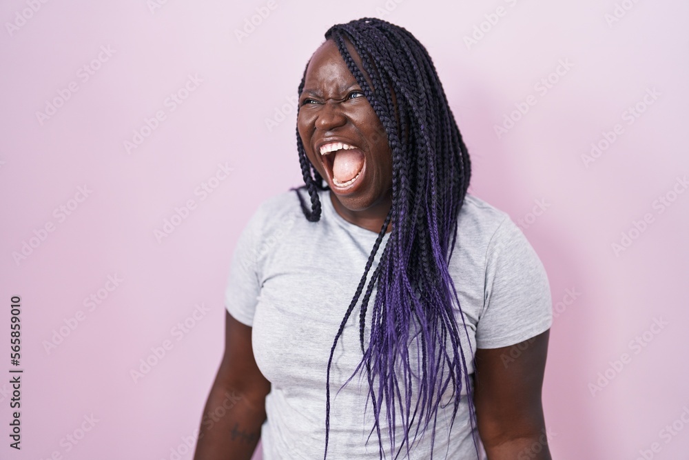 Poster young african woman standing over pink background angry and mad screaming frustrated and furious, sh