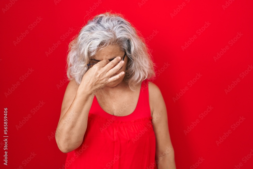 Poster middle age woman with grey hair standing over red background tired rubbing nose and eyes feeling fat