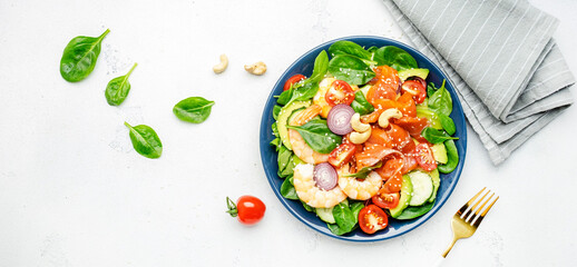 Ketogenic diet salad with salmon, shrimp, avocado, spinach, cucumber, tomato, cashew nuts, sesame. Low-carbohydrate lunch rich in healthy fats. White table background, top view banner
