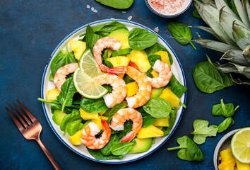 Shrimp pineapple salad with spinach, avocado and lime on blue kitchen table background, top view. Healthy vegetarian eating, balanced, clean diet food, weight loss dish