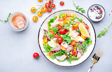 Tuna vegetables salad with cherry tomatoes, red onion, eggs, corn, paprika, lettuce, radicchio and arugula. Gray table background, top view