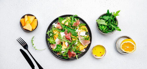 Gourmet lunch melon salad with cantaloupe, prosciutto, soft white cheese and arugula, olive oil and...