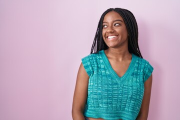 Fototapeta premium Young african american with braids standing over pink background looking away to side with smile on face, natural expression. laughing confident.