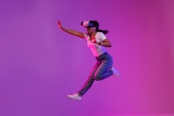 Excited Black Woman Wearing VR Glasses Jumping In Air In Neon Light