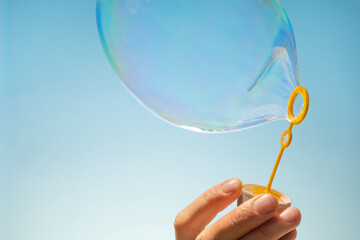 Close up side view shot of young man blowing soap bubbles on blue background. Focus on hands and...
