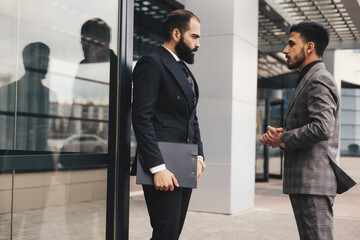 Business people outdoor meeting. Two men in suits are standing and talking to each other. Working break. Friendly conversation and business communication