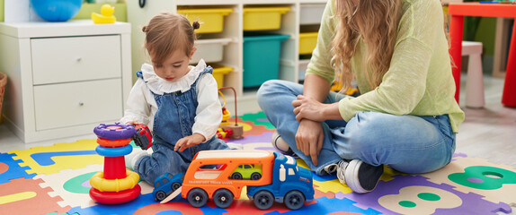 Teacher and toddler playing with cars toy sitting on floor at kindergarten