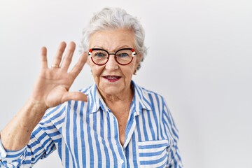 Senior woman with grey hair standing over white background showing and pointing up with fingers number five while smiling confident and happy.