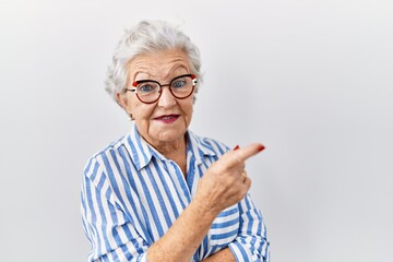 Senior woman with grey hair standing over white background with a big smile on face, pointing with hand and finger to the side looking at the camera.