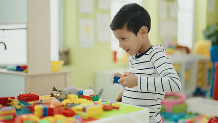 Adorable hispanic boy playing with construction blocks sitting on table at kindergarten