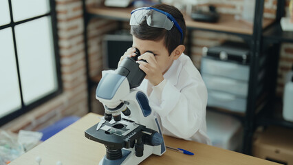 Adorable hispanic boy student using microscope at laboratory classroom