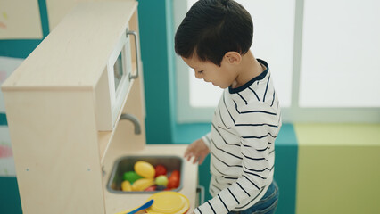Fototapeta na wymiar Adorable hispanic boy playing with play kitchen standing at kindergarten