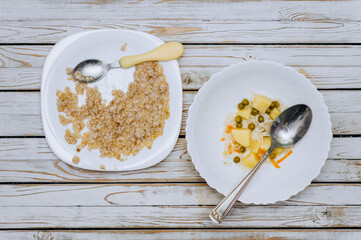 Leftovers from soup, porridge, uneaten food with bread crumbs lie on plates after a person on a wooden white table. Photography, concept, wooden background.