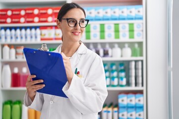 Young beautiful hispanic woman pharmacist writing on document at pharmacy