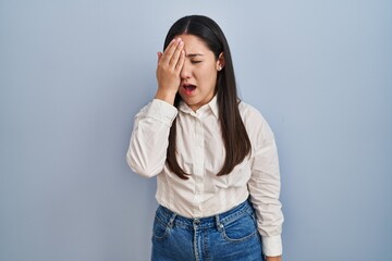 Young latin woman standing over blue background yawning tired covering half face, eye and mouth with hand. face hurts in pain.