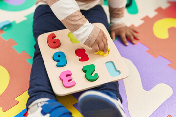 Adorable hispanic toddler playing with maths puzzle game sitting on floor at kindergarten