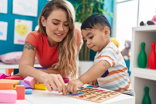 Teacher and toddler playing with maths puzzle game sitting on table at kindergarten