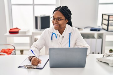 African american woman doctor using laptop writing medical report at clinic