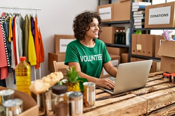 Young hispanic woman wearing volunteer uniform using laptop at charity center