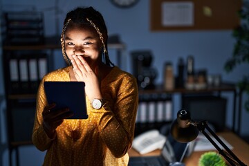 African american woman with braids working at the office at night with tablet laughing and...