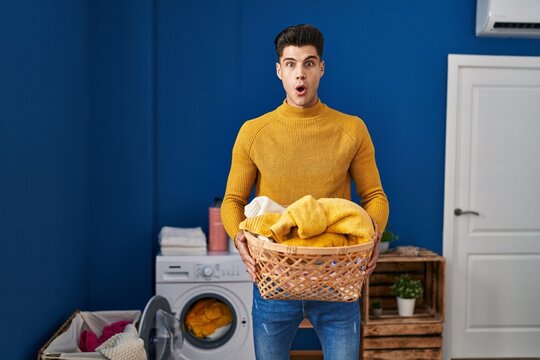 Young hispanic man holding laundry basket afraid and shocked with surprise and amazed expression, fear and excited face.
