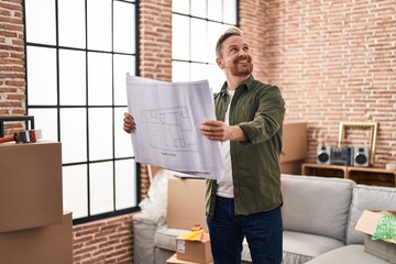 Young caucasian man smiling confident looking house plans at new home