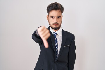 Young hispanic man with tattoos wearing business suit and tie looking unhappy and angry showing rejection and negative with thumbs down gesture. bad expression.