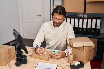 Middle age man ecommerce business worker using smartphone writing on package at office