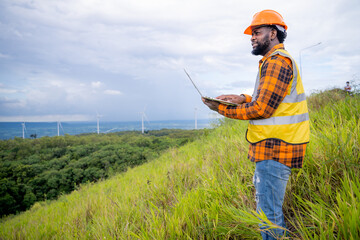 Portrait of engineer African American man working with laptop in wind turbine farm.