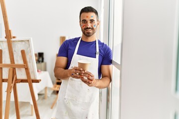Young hispanic man smiling confident drinking coffee at art studio