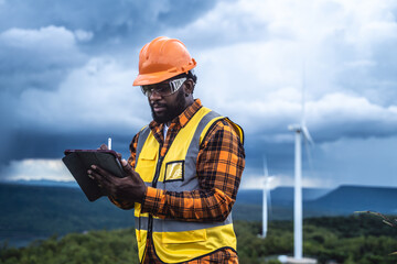 Portrait of engineer African American man working with laptop in wind turbine farm.