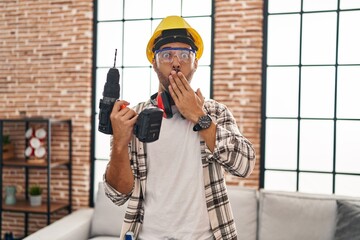 Young hispanic man with beard working at home renovation covering mouth with hand, shocked and afraid for mistake. surprised expression