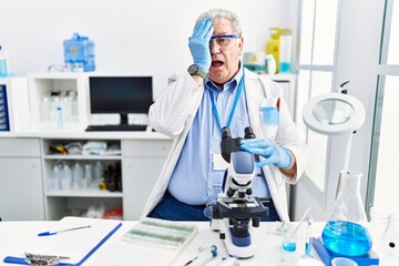 Fototapeta premium Senior caucasian man working at scientist laboratory covering one eye with hand, confident smile on face and surprise emotion.