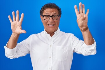 Middle age hispanic man standing over blue background showing and pointing up with fingers number...
