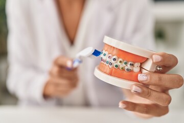 Young beautiful hispanic woman dentist teaching to clean tooth with brackets at clinic