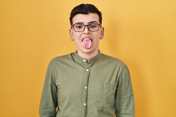 Obraz premium Non binary person standing over yellow background sticking tongue out happy with funny expression. emotion concept.