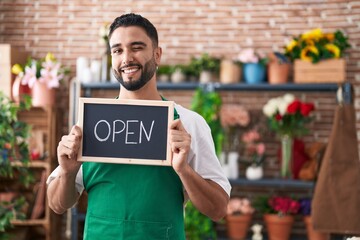 Hispanic young man working at florist holding open sign winking looking at the camera with sexy...