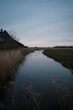 Canal on field by house against sky during dusk