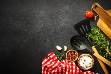 Food background. Kitchen utensils, wooden cutting board and food ingredients on black. Top view with copy space.