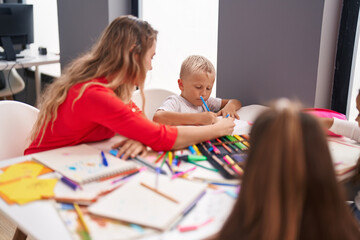 Teacher and toddler sitting on table drawing on paper at classroom